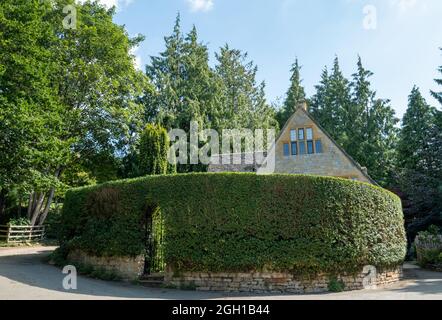 Attraente cottage in pietra participally oscurato dietro un'alta siepe scatola nel pittoresco villaggio di Cotswold incontaminato di Stanton in Gloucestershire Regno Unito. Foto Stock