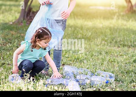 Pulizia dei bambini in una foresta. I bambini volontari puliscono la lettiera e mettono la bottiglia di plastica nel sacchetto di riciclaggio. Foto Stock