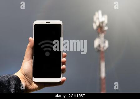 Una mano tiene un telefono cellulare sullo sfondo di una stazione di comunicazione senza fili. Trasferimento dati ad alta velocità. Tecnologie Foto Stock