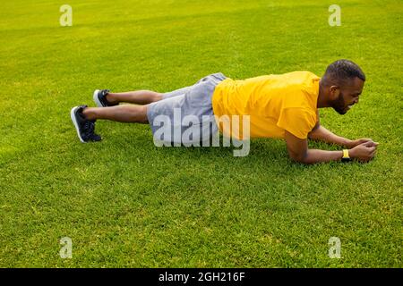 Vista laterale di un atleta afro americano concentrato che fa esercizio su un campo di erba. Giovane bel maschio che lavora duro, facendo l'allenamento mattutino Foto Stock