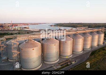 Odessa, Ucraina - Аugust 14, 2021: Terminali di grano del porto commerciale moderno del mare. Silos per immagazzinare grano in raggi di sole tramontato, vista dall'alto da quadrato Foto Stock