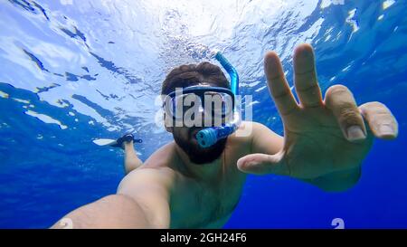 un uomo impegnato nello snorkeling sta nuotando nel regno sottomarino del mare rosso cercando di affiorare Foto Stock