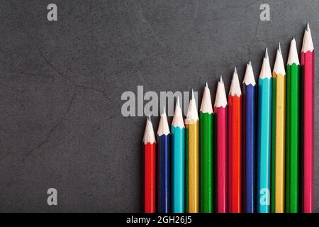 Matite di colori diversi in una fila su uno sfondo nero testurizzato. Vista dall'alto Foto Stock