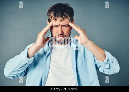 Un uomo di mezza età tiene le mani sulla testa. Il concetto di stress emotivo crisi e problemi. Studio ritratto di un europeo su sfondo grigio. Mal di testa e affaticamento. Foto Stock