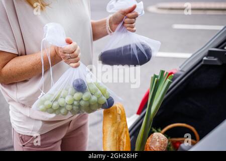 Niente sprechi e acquisti senza plastica. Donna che carica generi alimentari in sacchi a rete riutilizzabili nel bagagliaio dell'auto Foto Stock