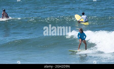 surfisti che prendono onde e si manovrano in mare in una limpida giornata estiva. Foto Stock