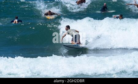 surfisti che prendono onde e si manovrano in mare in una limpida giornata estiva. Foto Stock