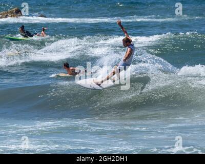 surfisti che prendono onde e si manovrano in mare in una limpida giornata estiva. Foto Stock