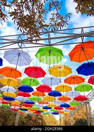 Ombrelloni a tema autunnale appendono sopra il vicolo del parco. Ombrelloni colorati appesi sopra gli alberi del parco Foto Stock