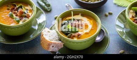 Vista stretta di ciotole di zuppa di zucca di butternut guarnito con verdure, pancetta e semi di zucca. Foto Stock