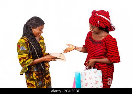 specialista africano di consegna che indossa un lonstraccio rosso con sacchetto di carta che tiene fuori la sua mano mentre il cliente di affari guarda la sua borsa Foto Stock