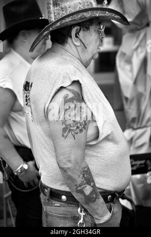 Un uomo con tatuaggi sul braccio si trova accanto allo stand di un artista in una mostra d'arte all'aperto a Santa Fe, New Mexico. Foto Stock
