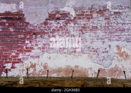 Sei chiodi arrugginiti bloccati in una trave di legno marcio di fronte ad un vecchio muro di mattoni Foto Stock