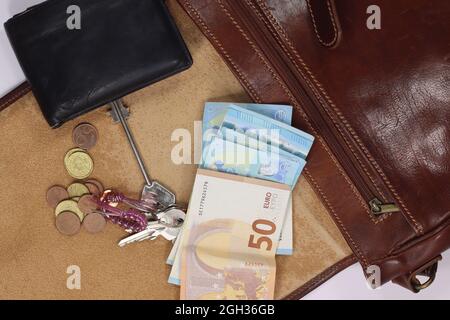 Scatto in testa di una borsa a spalla in pelle maschile aperta con contenuto di portafoglio e chiavi Foto Stock