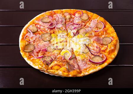 Una pizza rustica intera con cetriolo sottaceto, pancetta, anelli di cipolla e uova fritte viene servita su un piatto di carta su un tavolo di legno Foto Stock