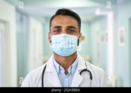 Medico indiano maschio che indossa il cappotto medico e la maschera facciale guardando la macchina fotografica. Foto Stock