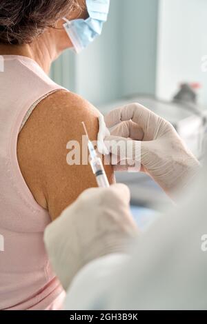Donna anziana che indossa la maschera per il viso che riceve l'iniezione della vaccinazione. Foto Stock