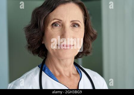 Sorridente medico donna anziano indossando un cappotto medico guardando la macchina fotografica. Verticale Foto Stock