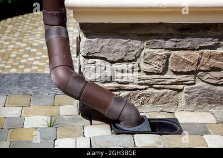 downpipe in pvc marrone drenaggio di plastica dell'acqua piovana dal tetto della casa al sistema di drenaggio a terra all'angolo della facciata dell'edificio rivestito di nat Foto Stock