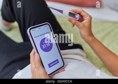 Primo piano delle mani di una donna che prende la sua temperatura basale Foto Stock