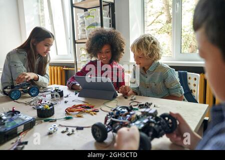 Ragazzi della scuola multietnica studenti che fabbricano auto robotizzate utilizzando un tablet. Foto Stock
