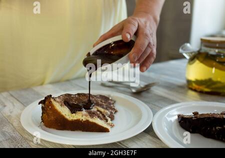 La donna aggiunge una guarnizione al cioccolato al dessert. Il processo di bere il tè con dolci fatti in casa. Foto Stock