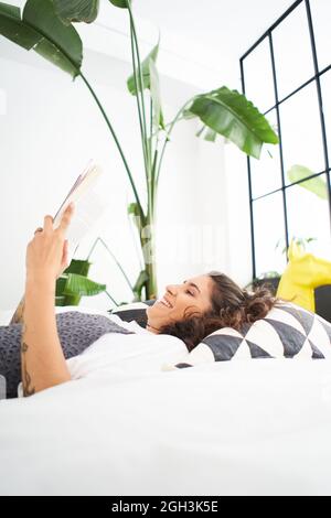 Giovane donna che legge un libro nella stanza accogliente, girare la pagina, imparare, studiare, istruzione, lettura di libri, concetto di soggiorno a casa e relax. Foto Stock