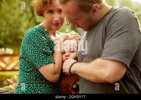 Crop cura madre e padre in casual vestire giocare con figlio carino mentre si trova insieme in zona rurale con lussureggianti alberi verdi Foto Stock