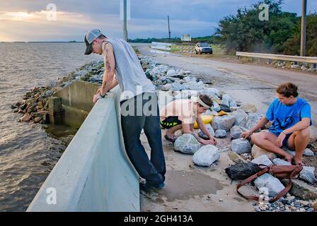 Un adolescente guarda su un ponte danneggiato mentre il suo amico lavora su una trappola a doppio anello di granchio dopo l'uragano Nate, 11 ottobre 2017, a Coden, Alabama. Foto Stock