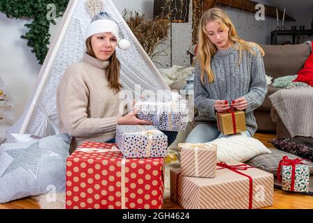 giovani ragazze che hanno divertimento che avvolge i regali a casa, grande lavoro di squadra di amici che impacchettano i regali per natale, prepari per il nuovo anno e le feste di natale Foto Stock