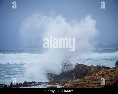 Spruzza da un'onda che si schiantava sulla costa rocciosa a Hermanus, Whale Coast, Overberg, Western Cape. Sudafrica. Foto Stock