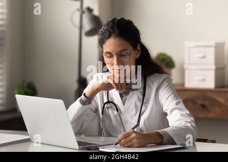 Medico del GP sorridente concentrato che dà la consultazione in linea della distanza sul laptop Foto Stock