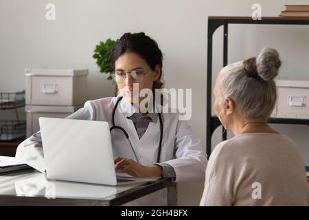 Grave giovane donna medico incontro con anziano in ufficio Foto Stock