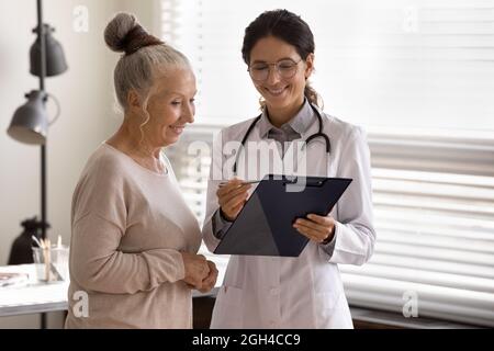 Terapista felice GP mostrando il cuscinetto per maturo 70s paziente femminile Foto Stock