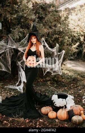 Halloween Witch redhead donna facendo stregoneria con magic Libro di incantesimi, magia nelle sue mani. Bella giovane donna in streghe cappello conjuring. Spooky Foto Stock