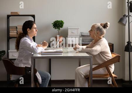 Medico positivo e paziente anziano incontro e parlare in ufficio Foto Stock
