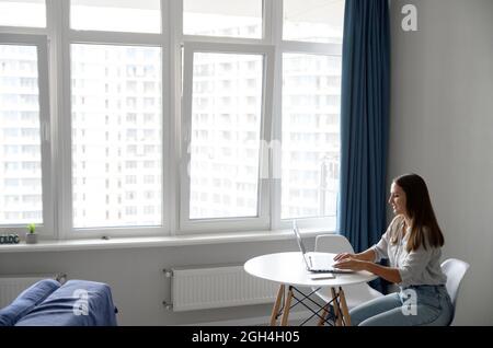 Giovane e intelligente freelance donna seduta con laptop in un accogliente appartamento moderno, studiare da casa, scrivere e-mail, lavorare al progetto da casa, navigare in internet Foto Stock