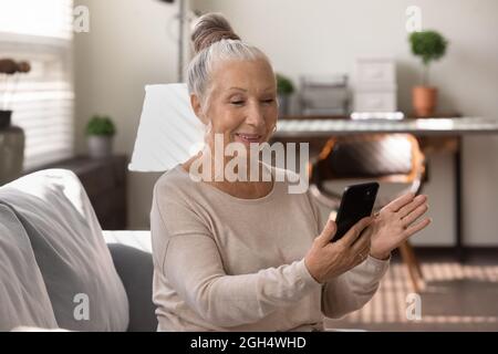 Signora felice anziana che usa lo smartphone a casa, videochiama Foto Stock