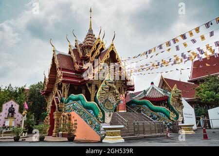 Bangkok, Thailandia 04.28.2021 Guardian Nagas, bandiere ed edifici colorati decorati segnano l'entrata della strada al Wat Nak Prok, il Tempio di Naga. Foto Stock