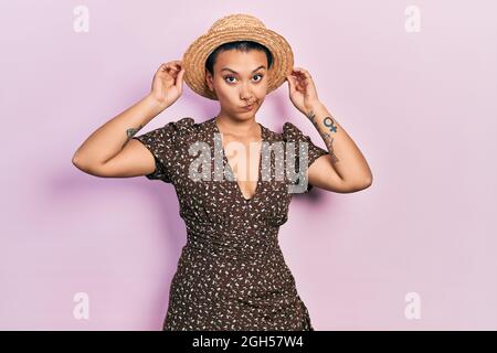 Bella donna ispanica con i capelli corti che portano il cappello estivo scettico e nervoso, rondante sconvolto a causa del problema. Persona negativa. Foto Stock