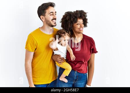 Giovane famiglia interrazziale di madre nera e padre ispanico con figlia che guarda via a fianco con sorriso sul viso, espressione naturale. Ridendo confi Foto Stock