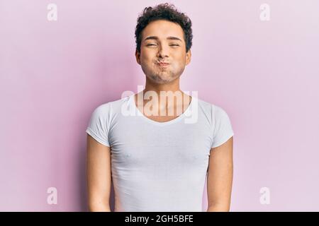 Giovane uomo bello che indossa casual maglietta bianca che soffia guance con faccia divertente. Bocca gonfia di aria, espressione pazza. Foto Stock