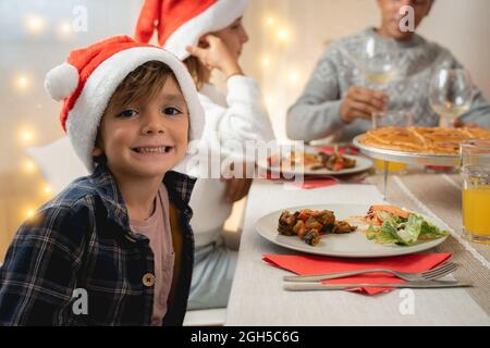 La famiglia felice festeggia il Natale insieme a una cena vegana al coperto a casa - Focus on boy face Foto Stock