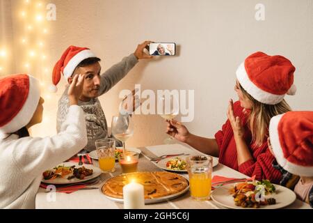 Famiglia felice che fa festa di video chiamata di Natale con la nonna anziana sul telefono mobile durante la celebrazione della cena vegana - fuoco sulla faccia della madre Foto Stock
