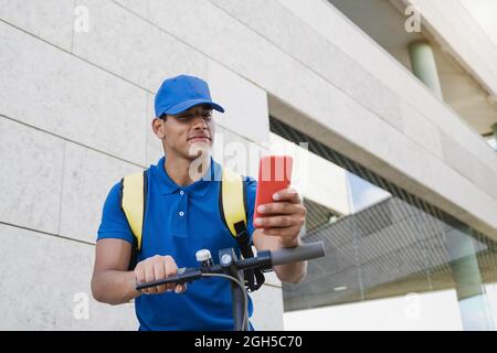 Corriere che fa servizio veloce di consegna del cibo usando il telefono mobile e lo scooter elettrico - consegna concetto di affari di trasporto - fuoco sulla faccia Foto Stock