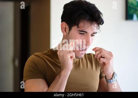 Giovane uomo che usa i denti per la pulizia del filo interdentale Foto Stock