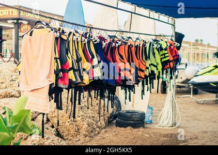 Una serie di giubbotti colorati per sport acquatici appendono sulla spiaggia Foto Stock