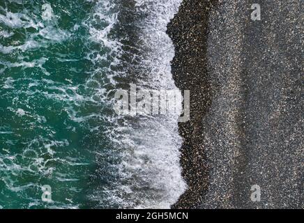 Le onde del mare verde si infrangono sulla sabbia nera e sulla spiaggia di ciottoli, la texture marina aerea Foto Stock