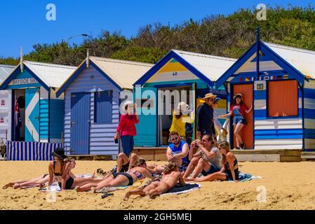 Le persone che si divertono sulla spiaggia di Brighton con le scatole da bagno colorate come sfondo a Melbourne, Victoria, Australia Foto Stock