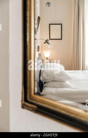 Interno di una camera da letto moderna con letto morbido con cuscini che si riflettono nello specchio appeso alla parete Foto Stock